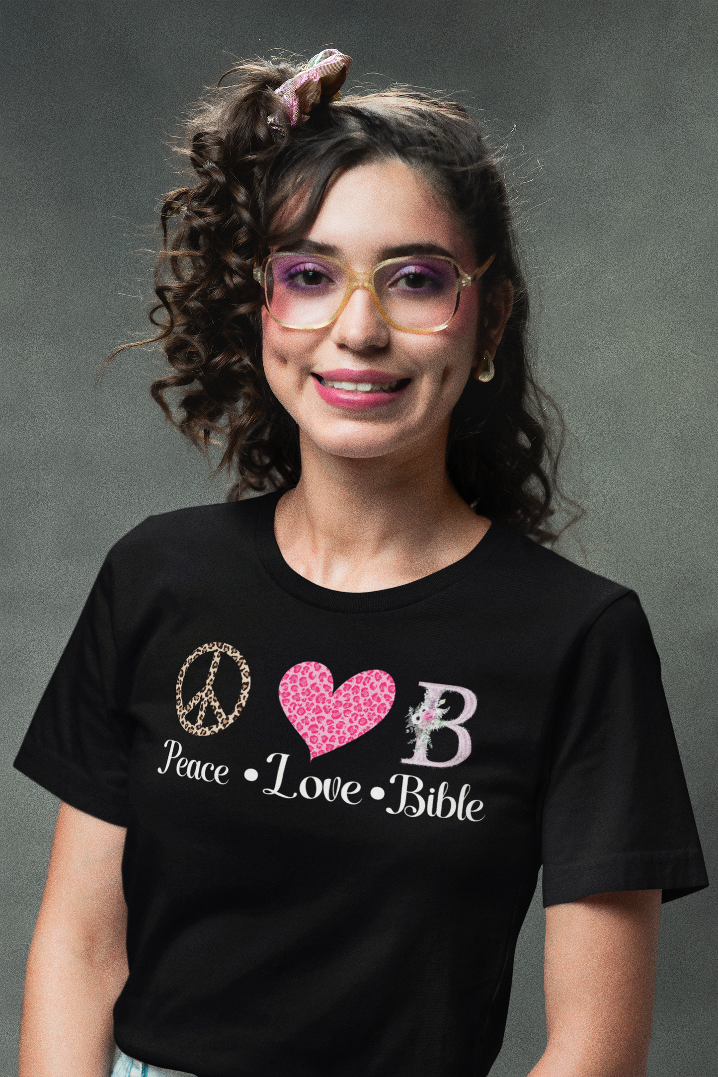 smiling woman wearing tee with leopard skin peace symbol, a pink heart symbol and a fancy letter B and reads-Peace, Love, Bible- Christian women's t-shirt, Bible tee, Religious gift, gift for mom, teacher gift, Peace sign tee, heart tshirt,,